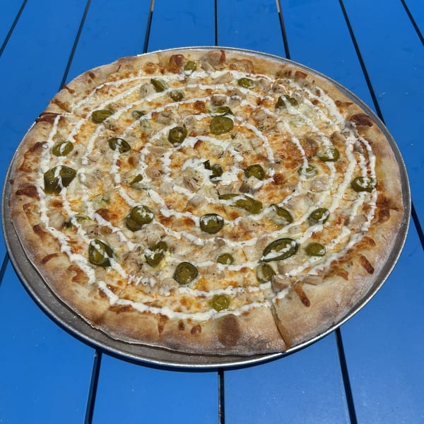 Shore Shack Pizza's chicken and jalapeño pizza with a white sauce drizzle on a blue table.