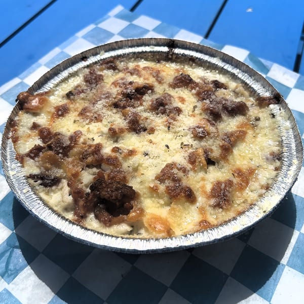 Baked pasta with melted cheese and meat in a foil tin on a blue and white checkered paper.