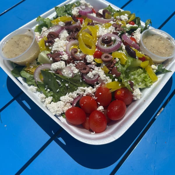 Shore Shack Pizza's large Greek salad with feta, olives, red onions, and tomatoes, with two dressing cups.