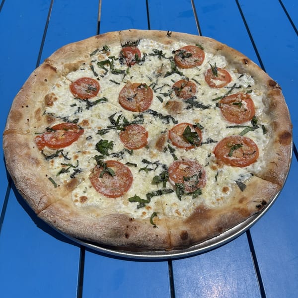 Shore Shack Pizza's white pizza with sliced tomatoes, fresh basil, and parmesan on a blue table.
