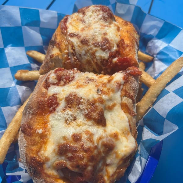 Two Shore Shack Pizza calzones with melted cheese and sauce, served with fries in a blue checkered basket.