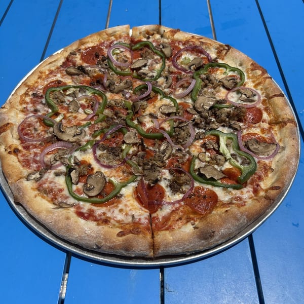 Shore Shack Pizza with pepperoni, sausage, mushrooms, green peppers, and red onions on a blue table.