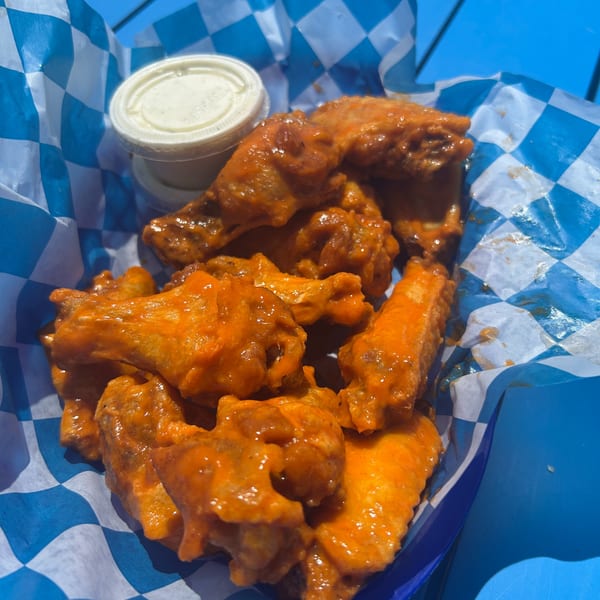 Shore Shack Pizza's buffalo wings, coated in orange sauce, served in a blue and white checkered basket.